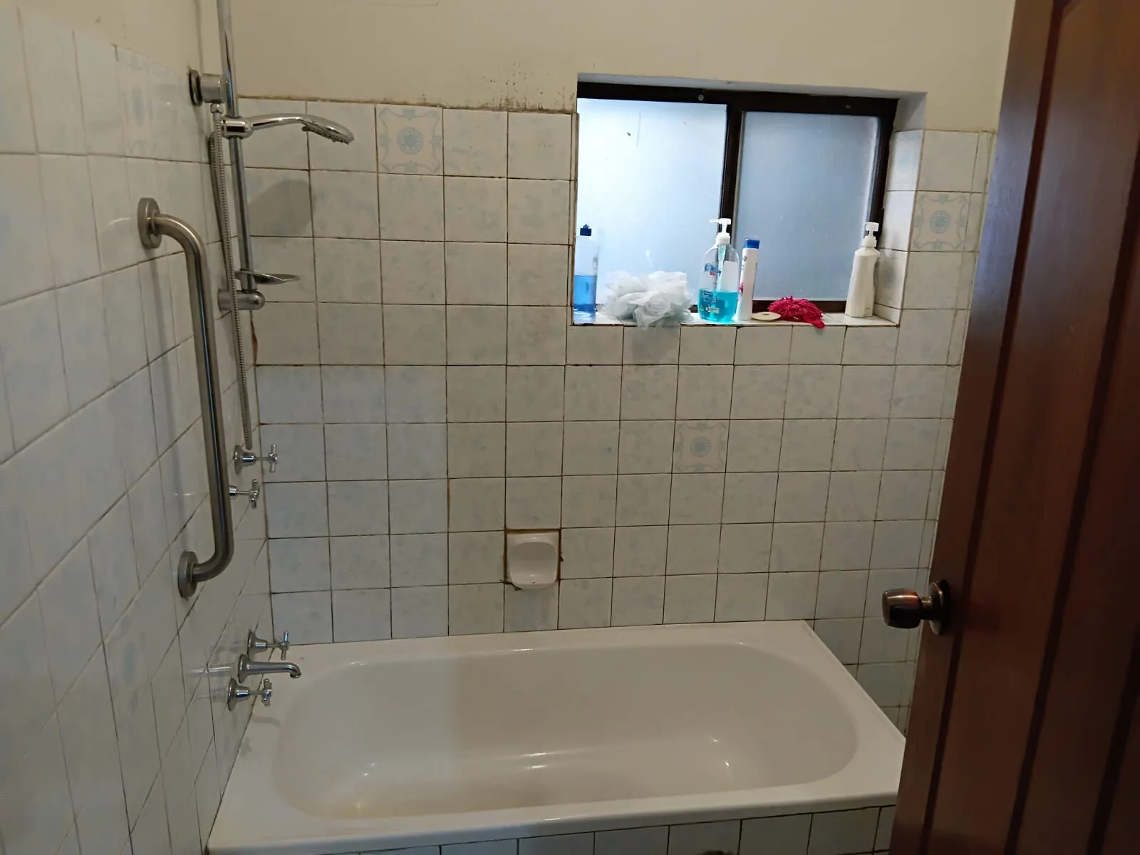 The bathroom at Mascot House with a bath, shower and grab rail.
