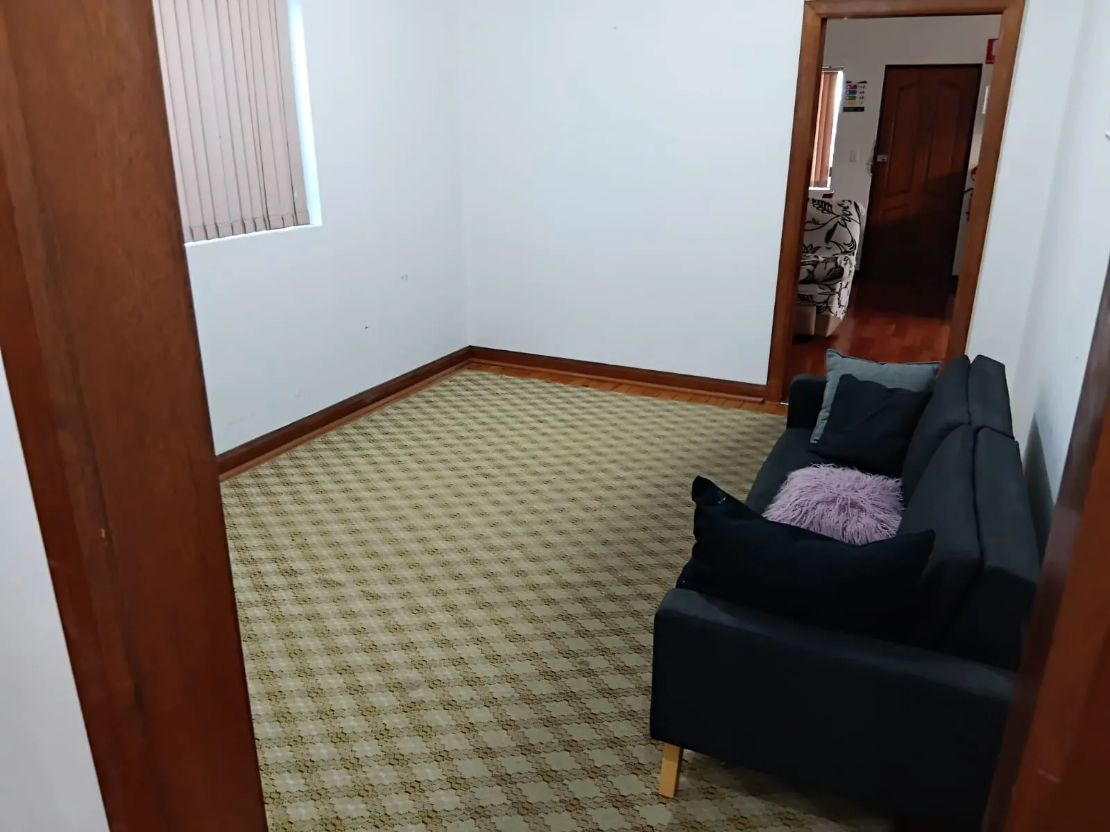 The lounge at Mascot House with a black sofa and a window with blinds.
