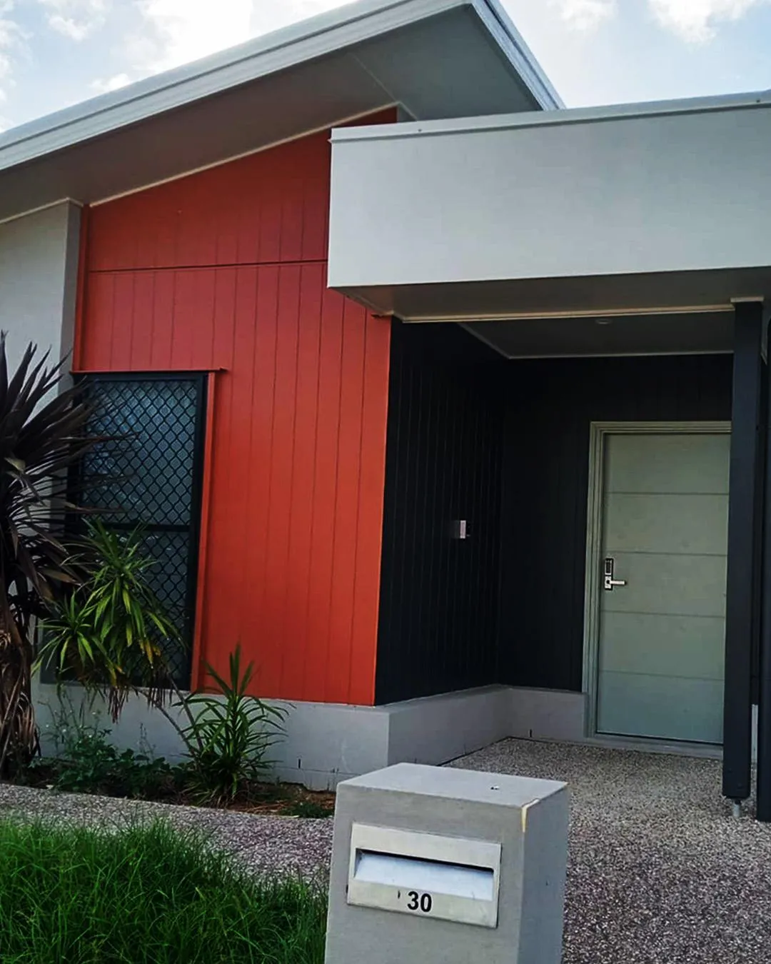 A contemporary home in Bahrs Scrub with a striking red feature wall, sheltered entry and native plants.