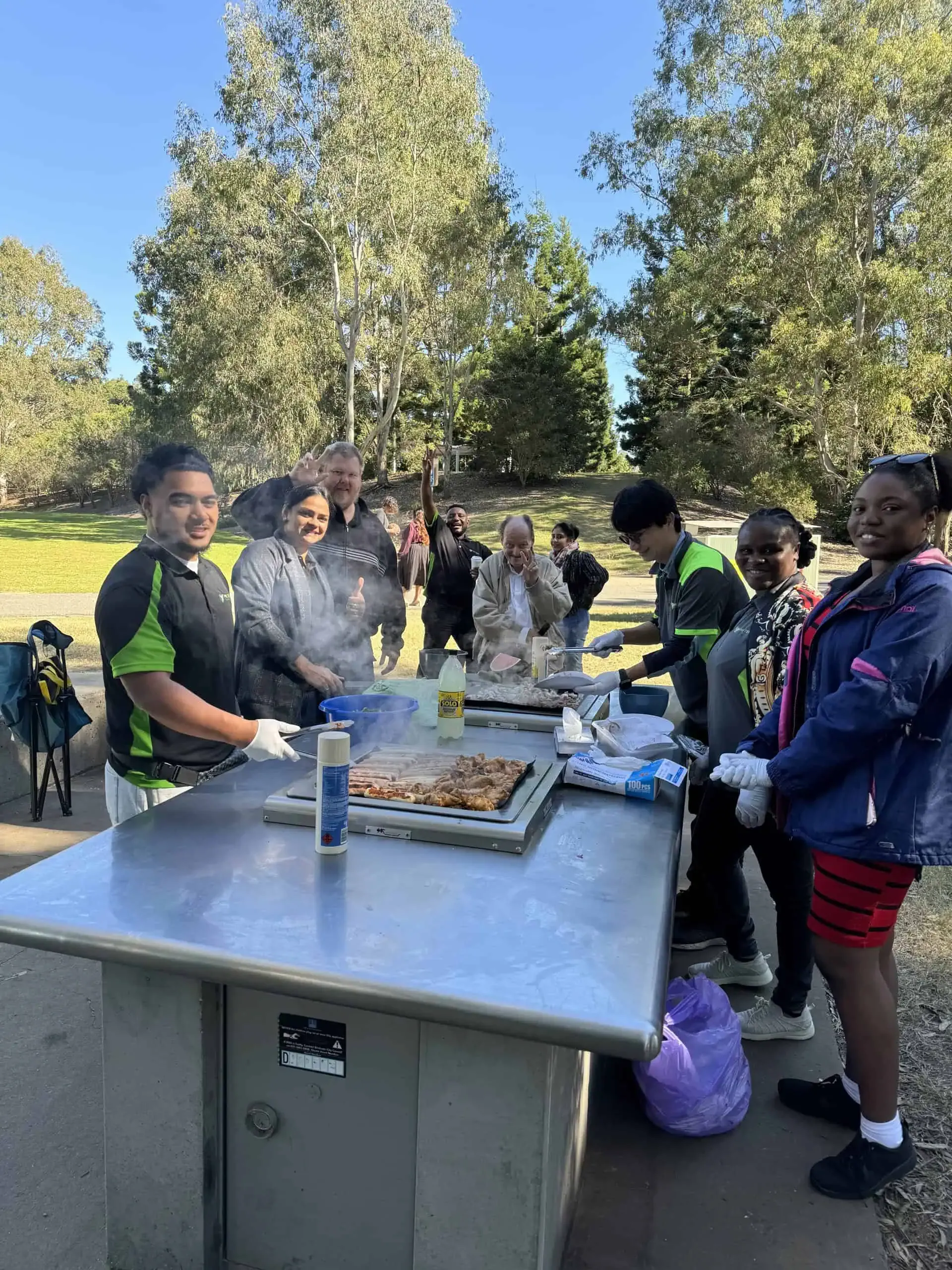 Participants and support workers cooking a barbecue together at a park.