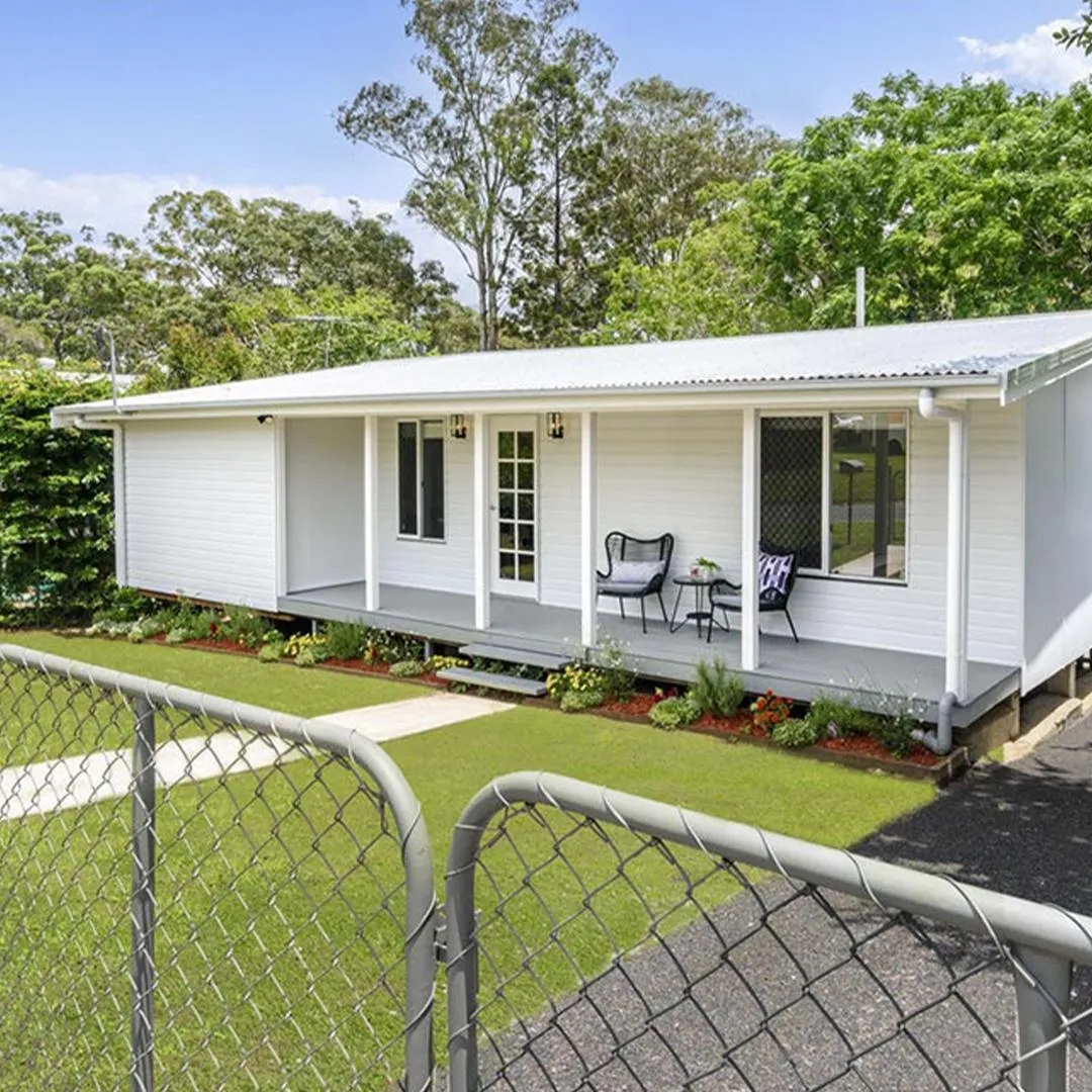 A white cottage in Caboolture with a long front veranda, cottage gardens and a big lawn.