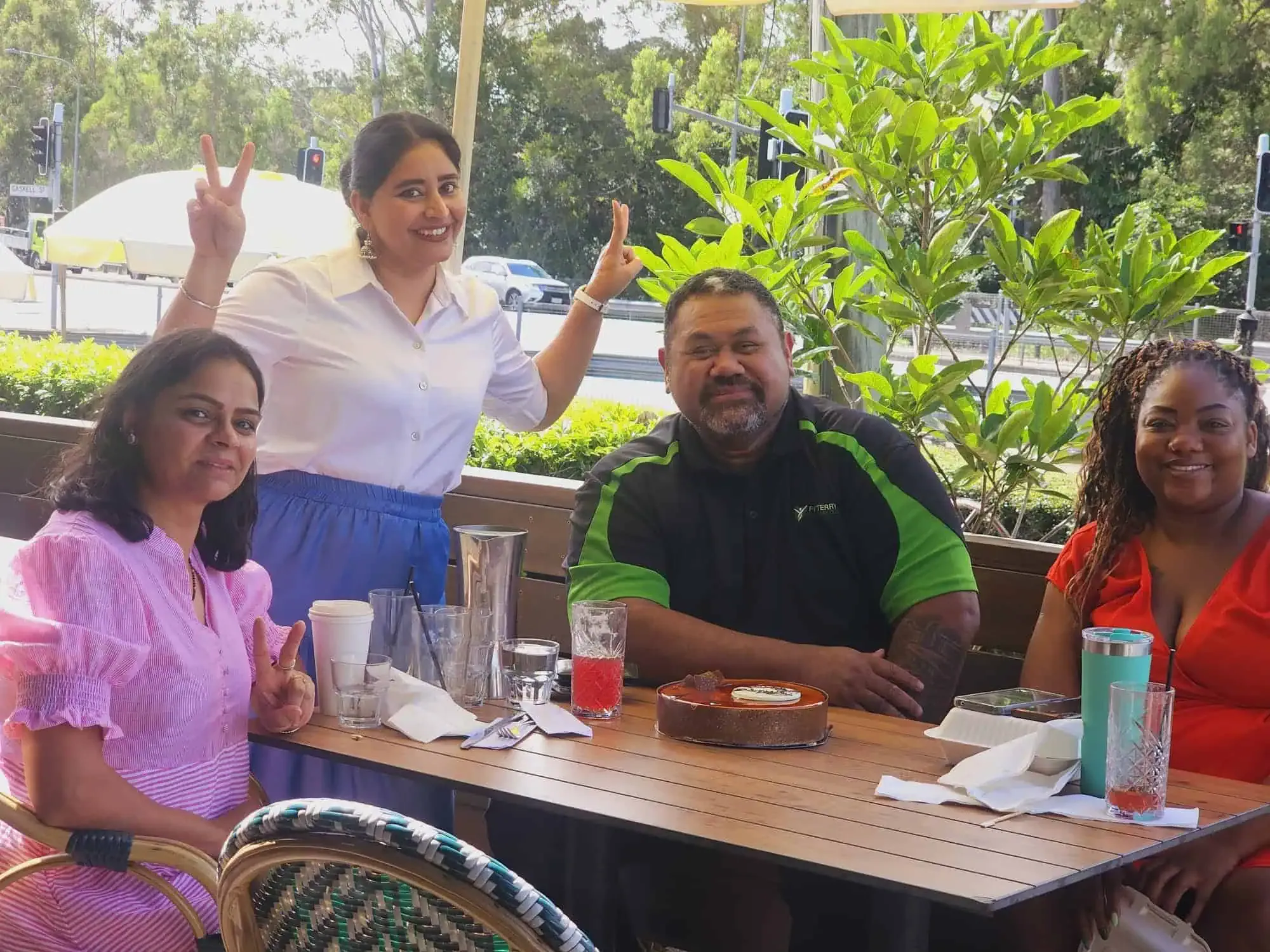 Participants and support workers sharing cake at a café table outdoors.