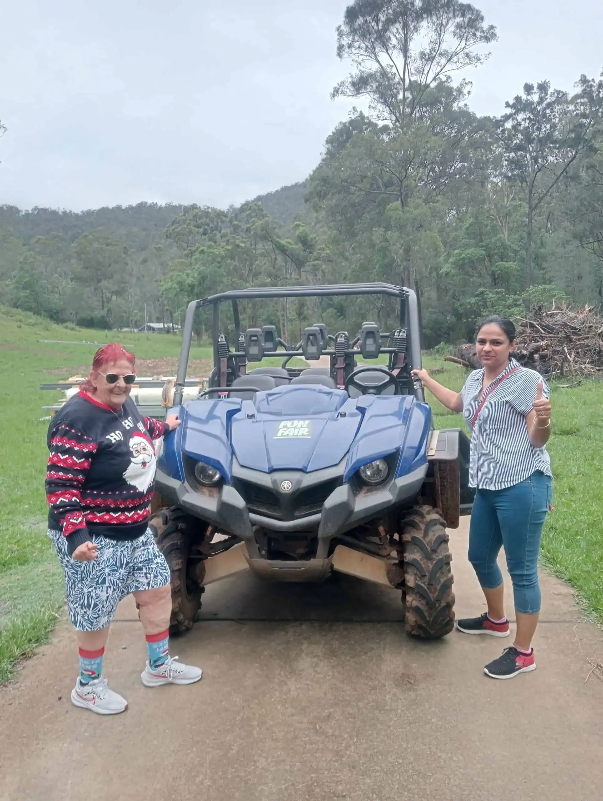 A participant giving a thumbs up beside a farm buggy with a support worker on a country outing.