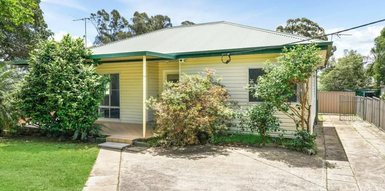A sunny weatherboard cottage with green trim, established gardens and a covered front patio in Kingswood.