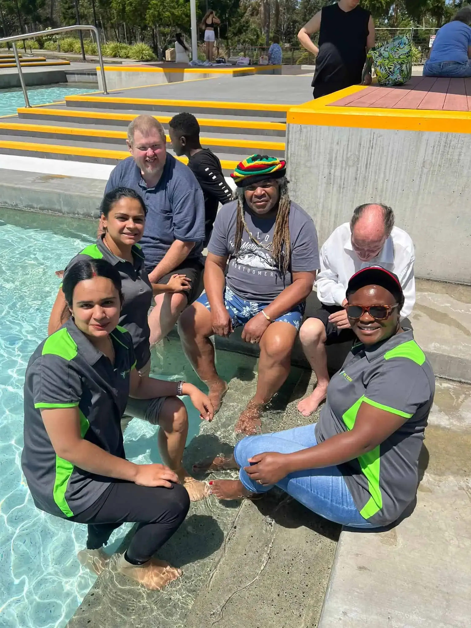 Support workers and participants cooling their feet together at a water park on a sunny day.